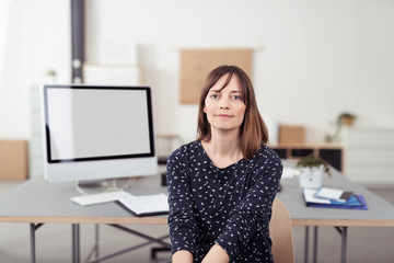 frau sitzt am schreibtisch in der firma mit pc im hintergrund