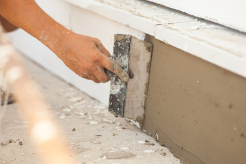 Man hand with trowel plastering a foundation of house - obrazy, fototapety, plakaty