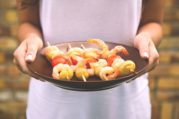 Kebab shrimp on a plate in the hands of a girl