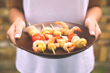 Kebab shrimp on a plate in the hands of a girl