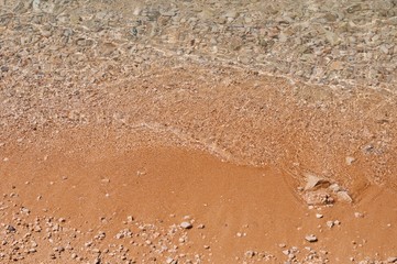 Fototapeta na wymiar Sandy beach with pebbles and wave as background