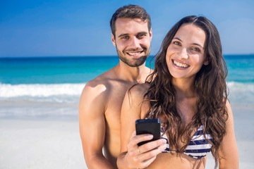 Smiling couple using smartphone at the beach