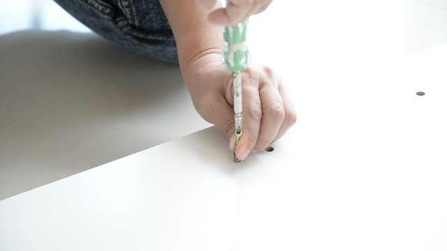 Woman's hand using a screw driver to screw in a white wood
