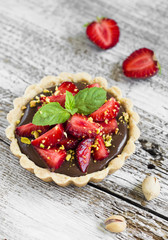 tartlet with chocolate cream, strawberries and pistachios on a light wooden background
