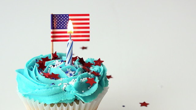 Patriotic American cupcake with flag and birthday candle that is lit and blown out.