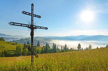 Fototapeta na wymiar Cross-crucifixion in the field on a sunny day with fog in the mo