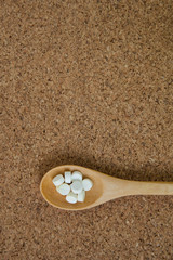 pills in a wooden spoon on a cork background.