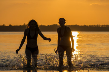 two teen girls have fun bathing in the sea in evening sun
