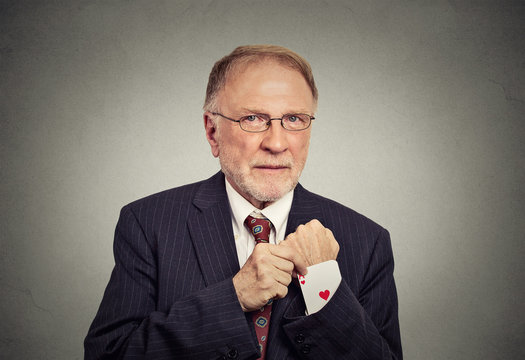 senior man pulling out a hidden ace card from suit jacket sleeve