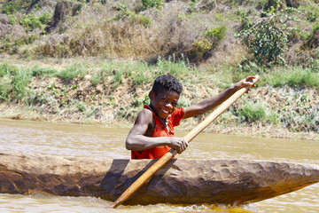 Young Malagasy african boy rowing traditional canoe on river