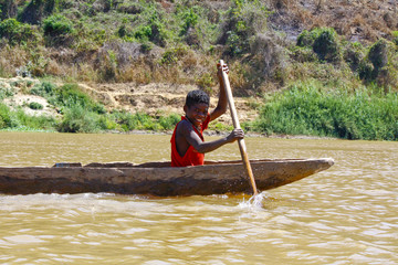 Young Malagasy african boy rowing traditional canoe on river