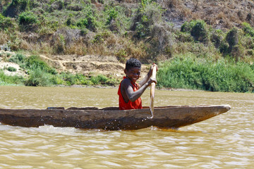 Young Malagasy african boy rowing traditional canoe on river