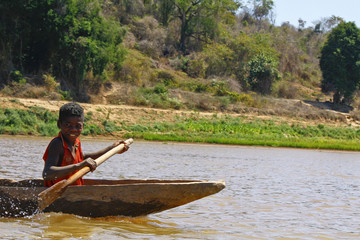 Young Malagasy african boy rowing traditional canoe on river