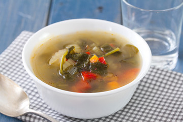 vegetable soup in white bowl with spoon and glass of water