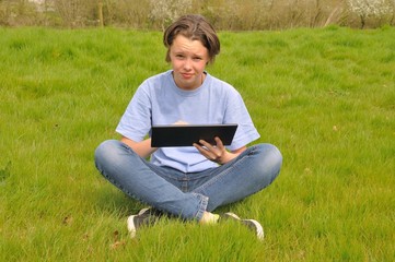 Naklejka na ściany i meble Girl sitting on the lawn and using digital tablet