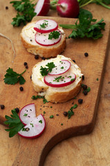 Sandwiches with fresh raddish and parsley leaves on a cutting board, wooden background