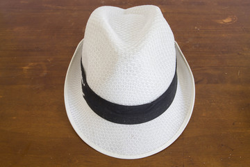 White hat with a hatband on a wooden table against dark background