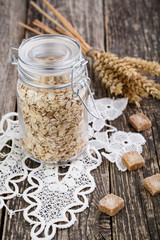The oat flakes in jar with sugar on lace napkin.