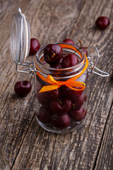 Jar with ribbon and fresh cherries on wooden table.