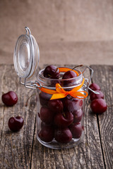 Jar with ribbon and fresh cherries on wooden table.