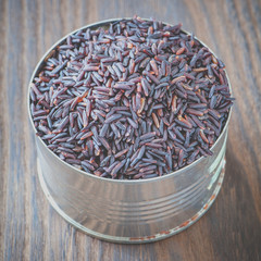 Uncooked brown rice in tin can on wood table background