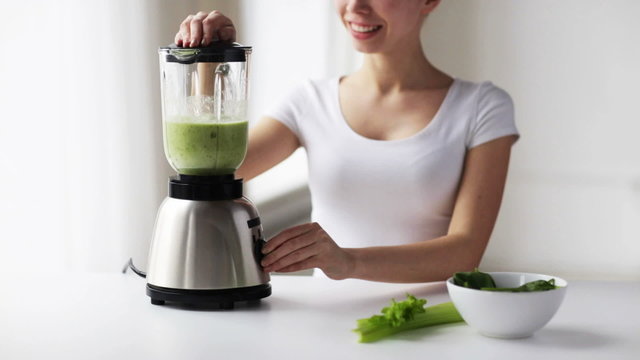 smiling woman with blender and green vegetables