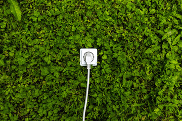 Weiße Steckdose mit Kabel auf grüner Wiese