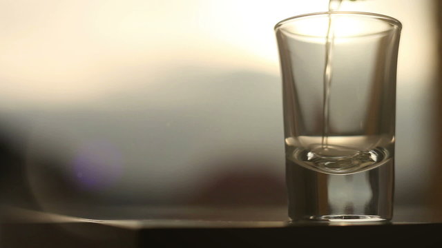An act of pouring a golden drink to the glass on the sunset background