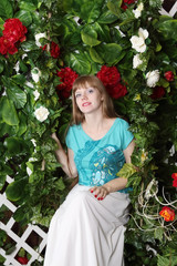 Beautiful young woman sits on swing among ivy with flowers