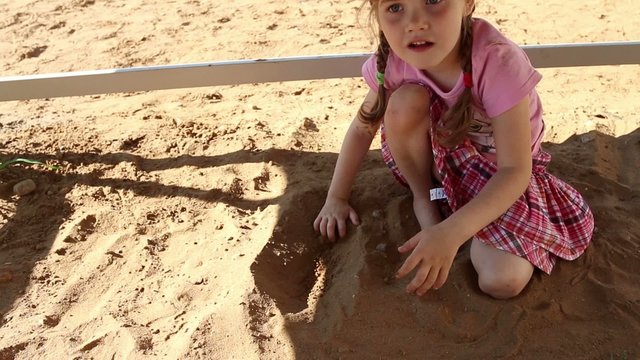 Happy little girl in pink plays with sand on playground at summer
