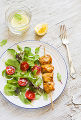 chicken skewers and fresh vegetable salad with cherry tomatoes and spinach on a light wooden background