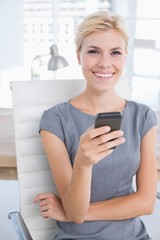 Smiling businesswoman sending a text at her desk