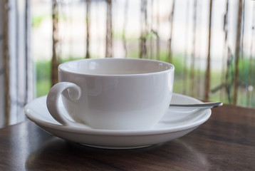 Blank white cup with a teaspoon on the table in a cafe