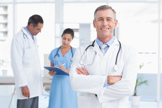 Doctor looking at camera while his colleagues works