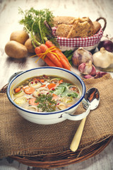 Vegetable soup in a metal bowl on a rural rustic wooden table.