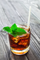 Glass of cola with ice and fresh mint on wooden table.