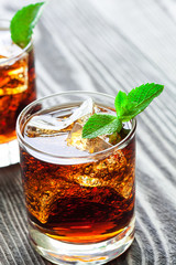Two glasses of cola with ice and fresh mint on wooden table.