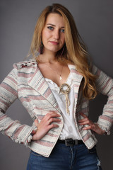 the studio portrait of the smiling young girl with a side with a long fair hair of 25 years in a white blouse and a jacket on a neutral background, looks at the viewer