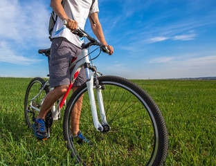 Young man riding on a bicycle on green meadow with a backpack