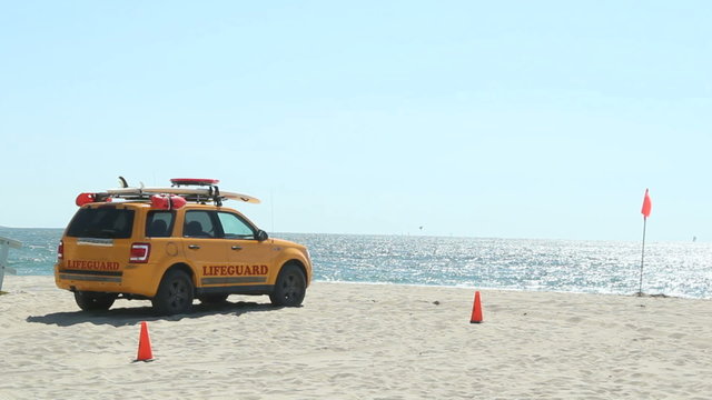Lifeguard SUV on the beach - Yellow baywatch lifeguard vehicle parked on the beach with full equipment, red flag is up, strong wind