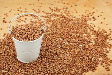 White bucket of buckwheat on the wooden floor