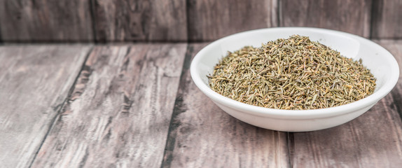Dried thyme herbs in white bowl over weathered wooden background