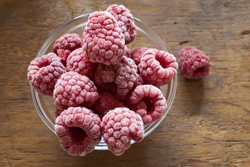 Tiefgefrorene Himbeeren in einer Glasschale auf Holztisch