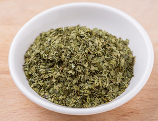 Dried parsley herb in white bowl over wooden background