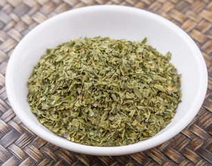 Fototapeta na wymiar Dried parsley herb in white bowl over wicker background