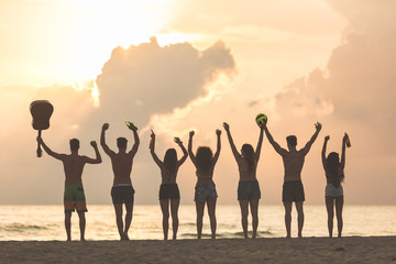 Fototapeta premium Group of friends raising hands on the beach at sunset