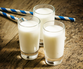 Three glasses of fresh milk on old wooden table in rustic style,