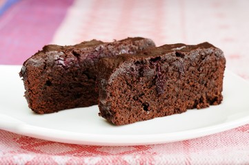 Two pieces of dark chocolate cake with cherries in white plate