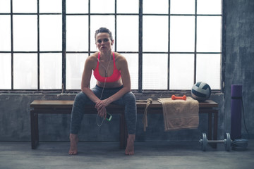 Woman sitting on bench by window in loft gym listening to music