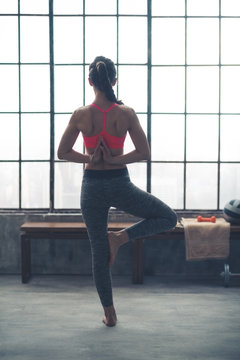 Rear View Of Woman Doing Yoga Tree Pose With Hands Behind Back